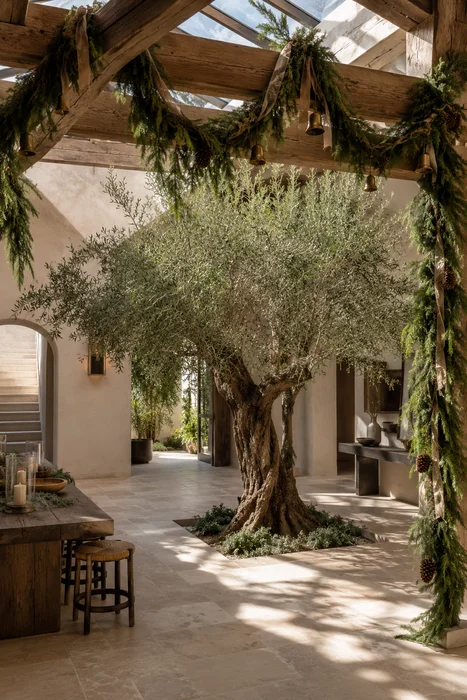 The Art of Styling Norfolk Pine Natural Touch Garland for Christmas 12 Evergreen garland with brass bells draped across timber beams in Mediterranean courtyard