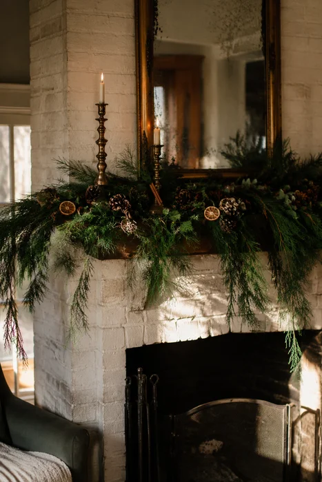 The Art of Styling Norfolk Pine Natural Touch Garland for Christmas 5 Evergreen garland with dried citrus and brass candlesticks on white brick fireplace